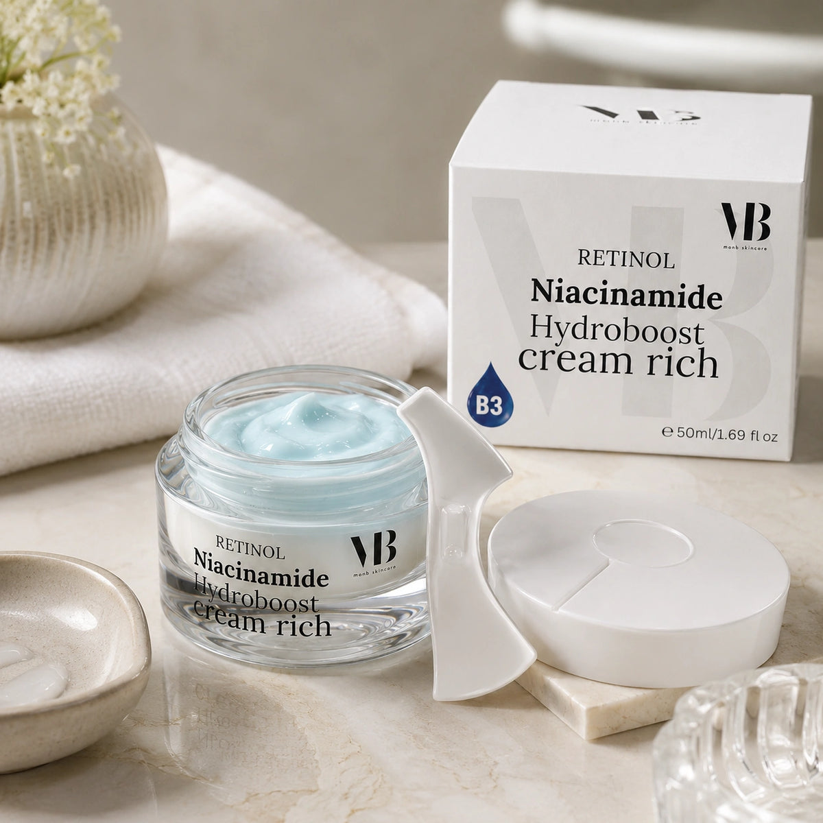 Geöffneter Tiegel der MOnB Retinol Niacinamide Hydroboost Cream Rich mit hellblauer Creme und Spatel für intensive Pflege und Feuchtigkeit